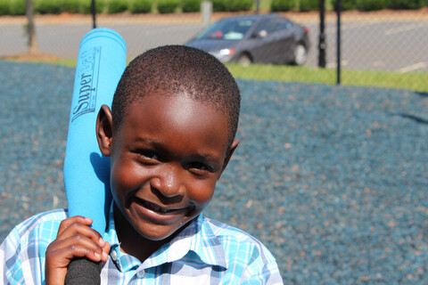 A boy smiling with a baseball bat in his hand