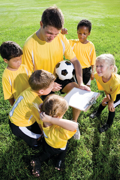 Coach with team of children playing soccer, 5 and 6 year old boys and girls